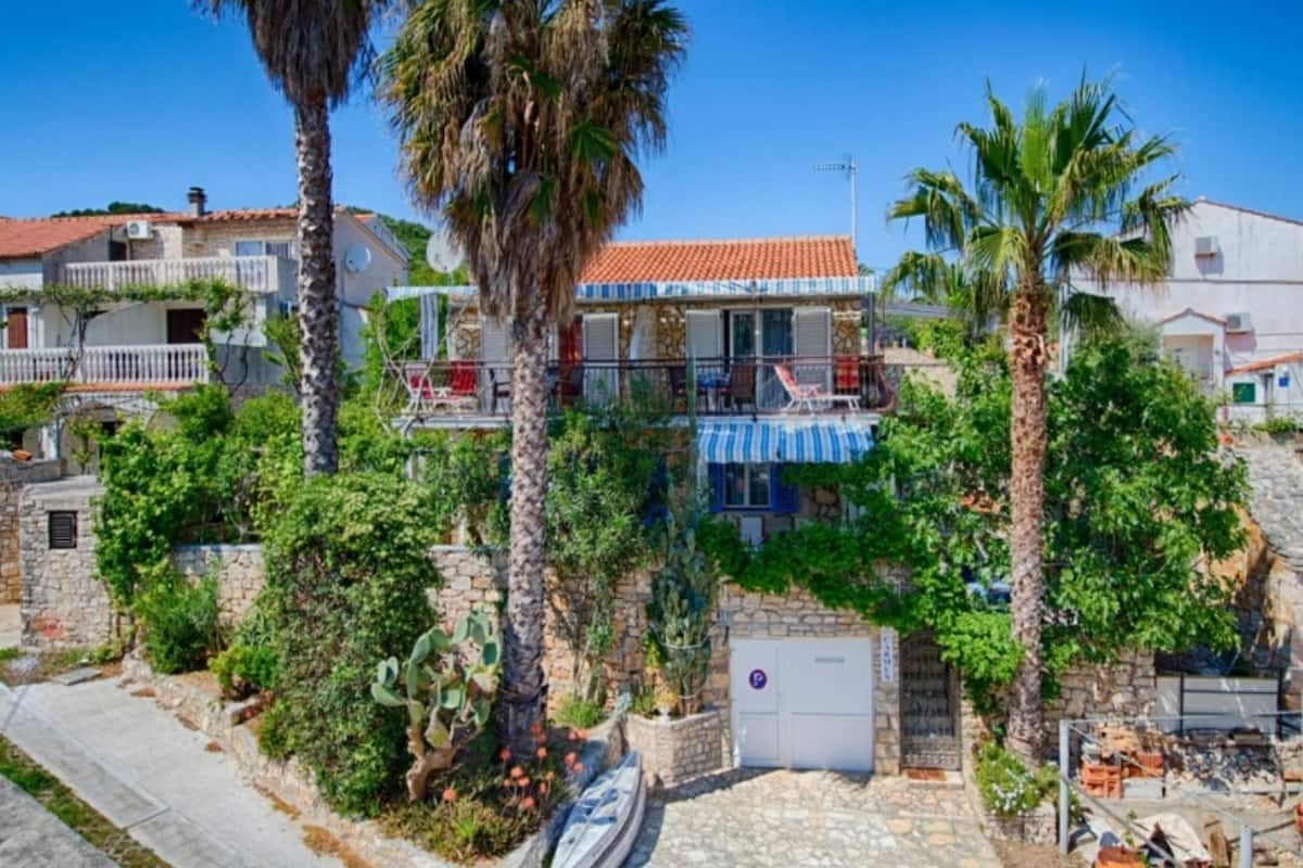 A coastal property with a stone facade, a balcony with red chairs, and a clear blue sky.