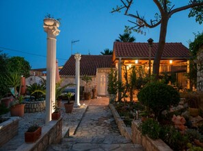 A stone pathway leading to a building with a tiled roof and a covered patio area. - Golden Coast Apartments (Vis)