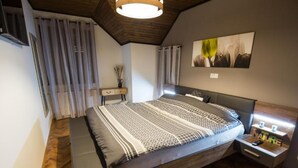 A modern bedroom with a large bed, wooden flooring, a nightstand with a lamp, and a painting on the wall. - Belajec Wine & Nature Retreat (Popovaca)