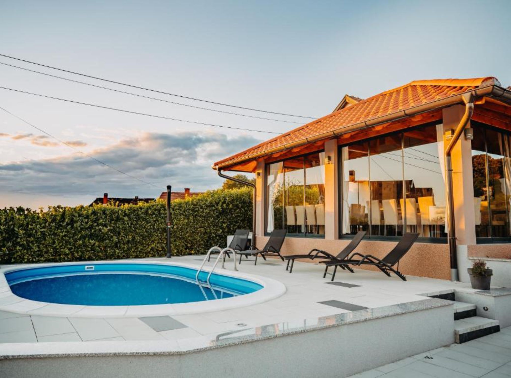 Un área de piscina moderna al aire libre, con una zona de estar cubierta y sillas de descanso.