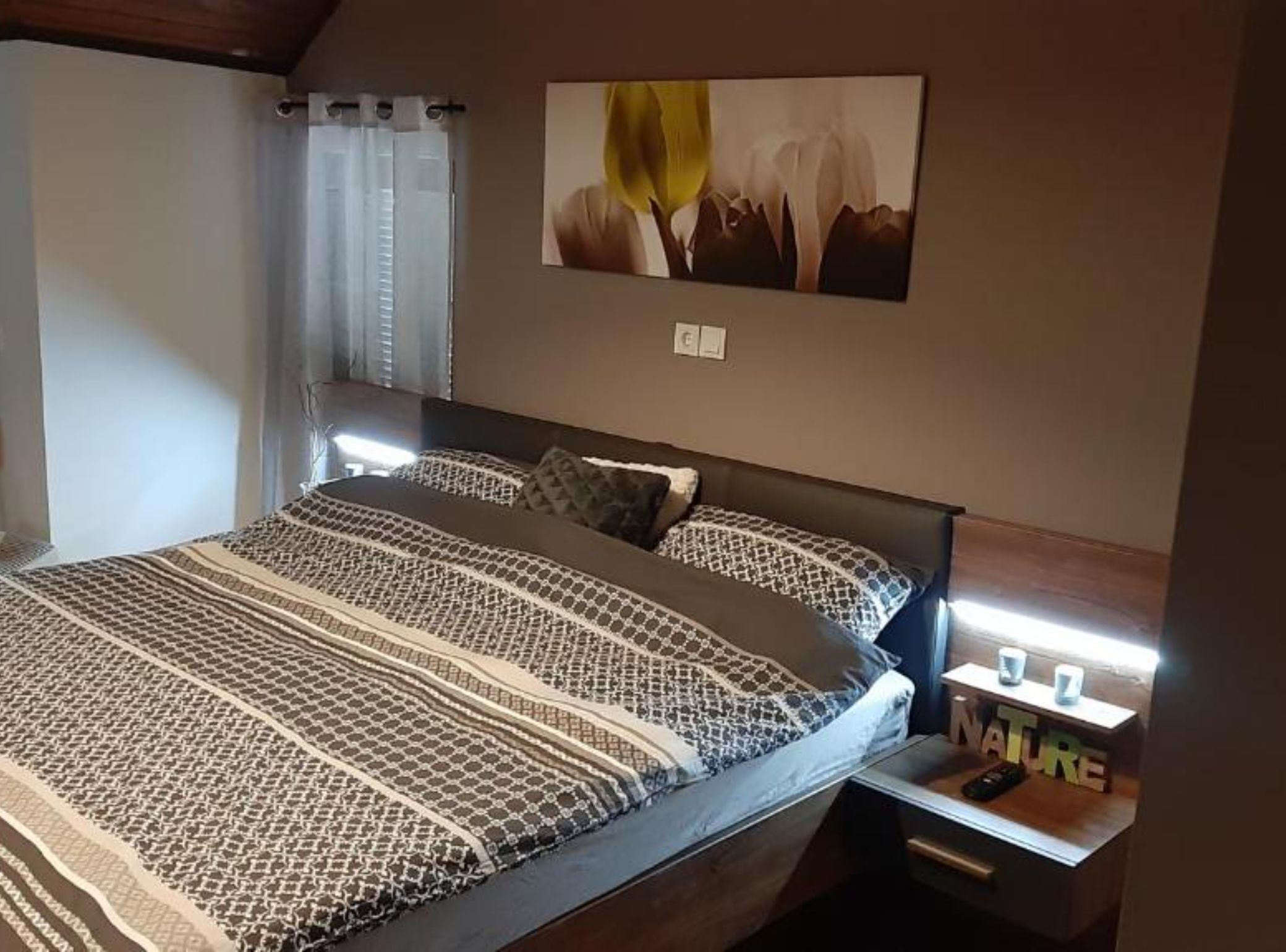 Une chambre à coucher avec une couvre-lit à motifs, une table de chevet avec une lampe et une œuvre d’art accrochée au mur.