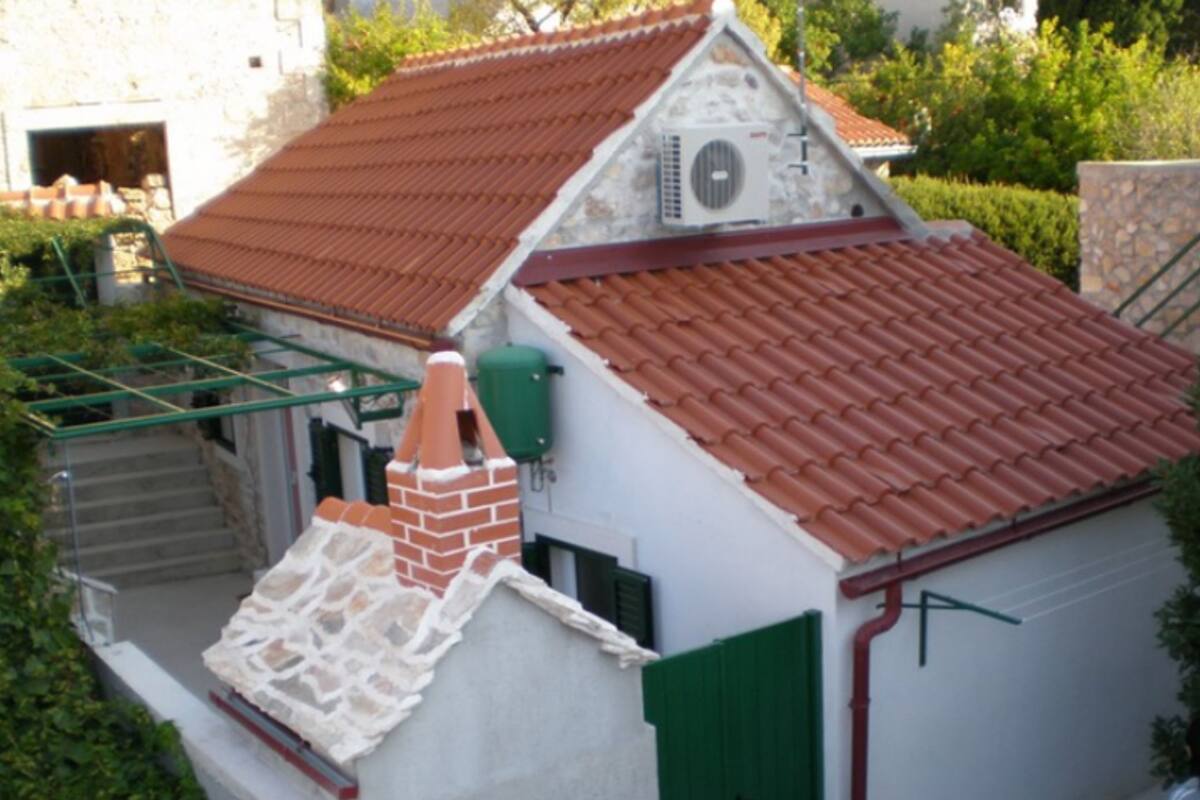 Un petit bâtiment avec un toit recouvert de tuiles rouges, une cheminée en briques et une porte verte.