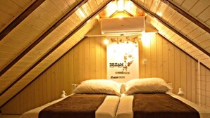 Una habitación con techo inclinado y paredes de madera, que incluye una cama con ropa de cama blanca y marrón, un equipo de aire acondicionado y un cartel en la pared.