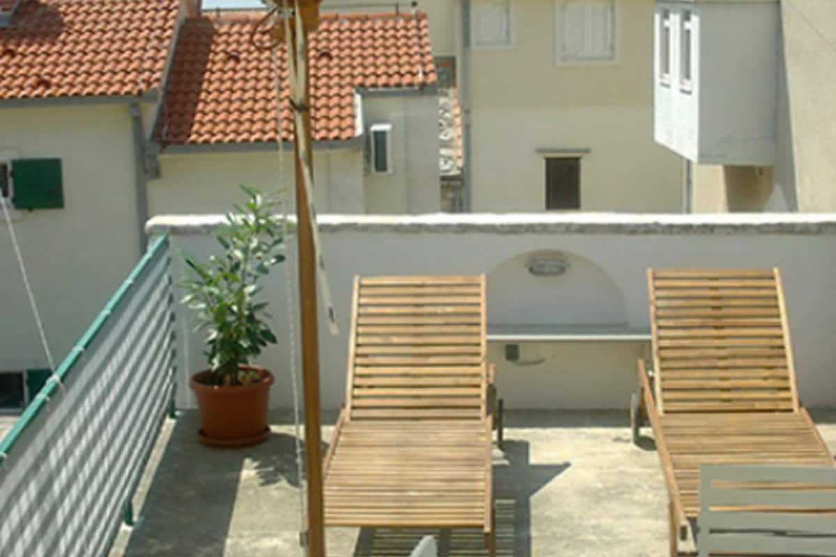 Une terrasse sur le toit, avec deux fauteuils en bois, un pot de fleurs et une rambarde en métal.