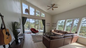 Ein geräumiges Wohnzimmer mit einer großen Couch, einem Schaukelstuhl, einer Gitarre und einem Deckenventilator.