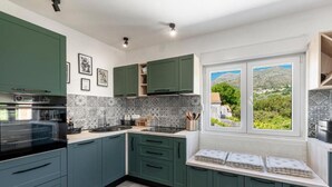 A modern kitchen with green cabinets, a built-in oven, and a window with a view of greenery. - Lux Holiday Home Maribu (Zupa dubrovacka)