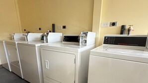 Μια σειρά από λευκά επαγγελματικά πλυντήρια σε ένα πλυσταριό με μπεζ τοίχους και μαύρο δάπεδο.