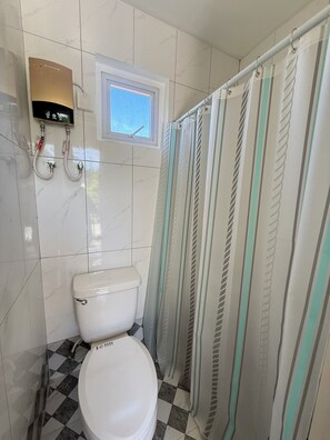 A bathroom with a toilet, a shower curtain, and a window.