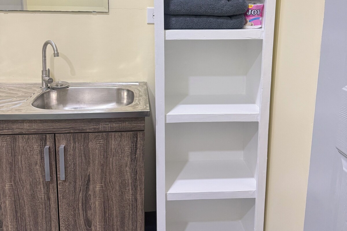 Une salle de bain avec un lavabo, des meubles en bois et un meuble de rangement blanc contenant des serviettes et des articles de toilette.