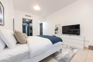A modern bedroom with a bed, a television, and a desk. - Bloomfields 1BR in Burooj Views - Al Reem (Abu Dhabi)