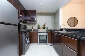 A modern kitchen with stainless steel appliances, wooden cabinets, and a black countertop. - Bloomfields 1BR in Burooj Views - Al Reem (Abu Dhabi)