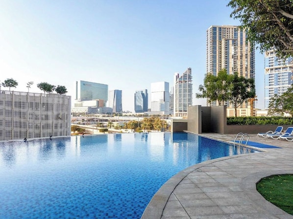 A swimming pool with a cityscape view, surrounded by high-rise buildings. - Bloomfields 1BR in Burooj Views - Al Reem (Abu Dhabi)