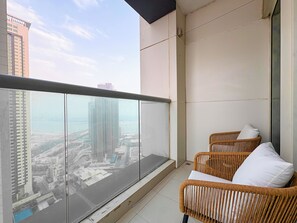 A balcony with a view of a cityscape, two wicker chairs with cushions, and a glass railing. - Bloomfields 1BR in Burooj Views - Al Reem (Abu Dhabi)