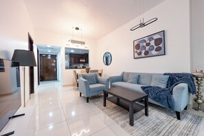 A modern living room with a sofa, coffee table, and a dining area in the background. - Bloomfields 1BR in Burooj Views - Al Reem (Abu Dhabi)