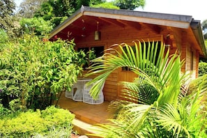 A wooden cabin with a porch, surrounded by lush greenery.