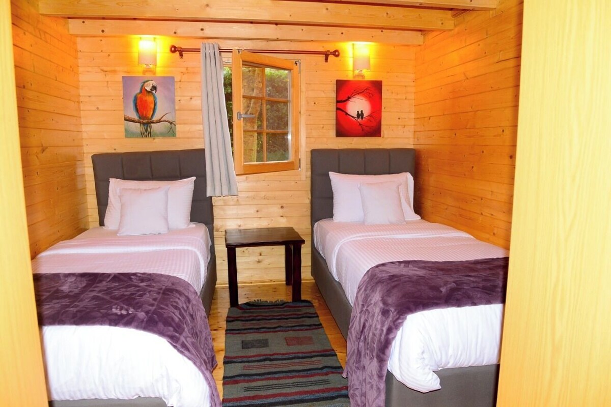 A wooden cabin room with two beds, a small table, and a window.