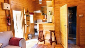Uma cabana de madeira compacta com cozinha compacta, área de refeições com banquinhos e sala de estar com sofá.