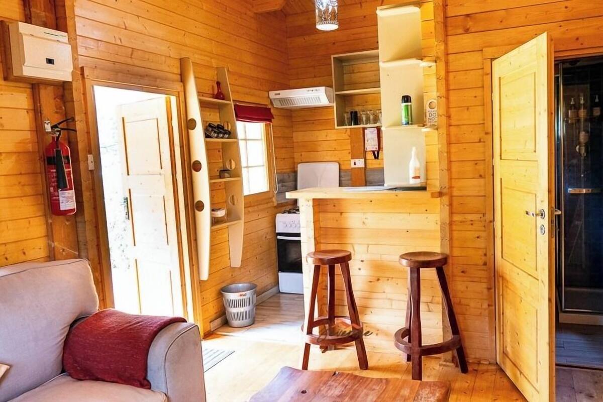 A compact wooden cabin with a kitchenette, a dining area with stools, and a living space with a sofa.