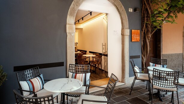An outdoor seating area with tables and chairs, an archway entrance, and a visible interior space with tables and chairs. - Il Vicolo Suite Apartments Cortiletto (Gardola)