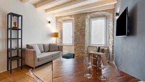 A modern living room with a wooden table, a sofa, a TV mounted on the wall, and a stone wall. - Il Vicolo Suite Apartments Cortiletto (Gardola)
