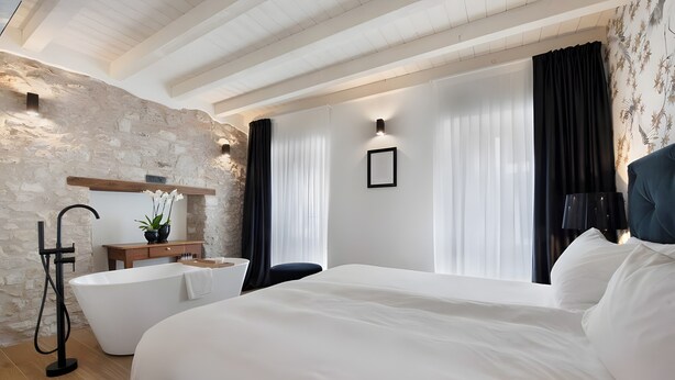 Ein modernes Hotelzimmer mit einem großen Bett, einer Badewanne, einem Holzanrichte und einer Steinwand.