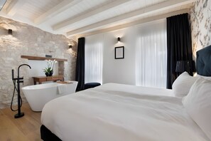A modern hotel room with a large bed, a bathtub, a wooden vanity, and a stone wall. - Apartment 'il corso' with Wi-Fi and air conditioning (Gardola)