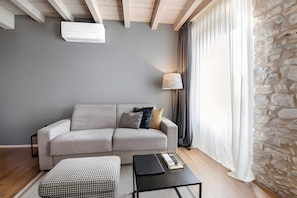 Ein modernes Wohnzimmer mit grauem Sofa, einem schwarzen Couchtisch, einem gemusterten Hocker, einer Lampe und einer Steinwand.