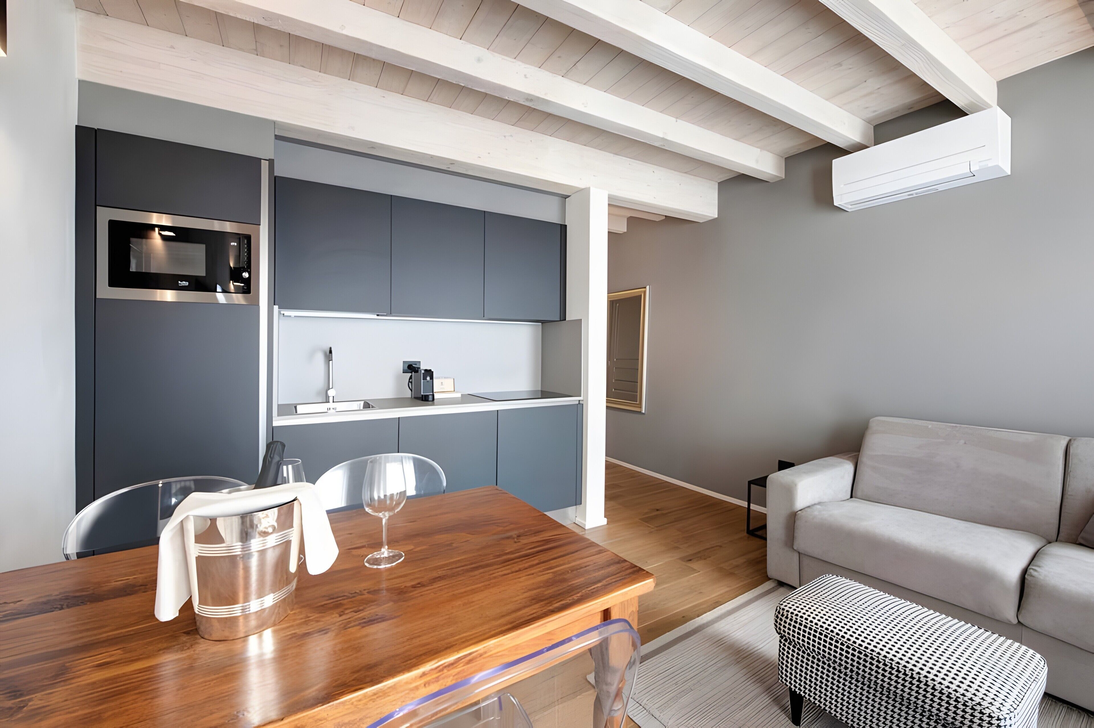 Eine moderne Küche mit integrierten Geräten, ein Essbereich mit Holztisch und -stühlen sowie ein graues Sofa.