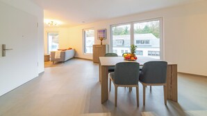 A modern living room with a sofa, a dining table with chairs, and a fruit bowl. - Halternative Residence Rose (Luxembourg City)