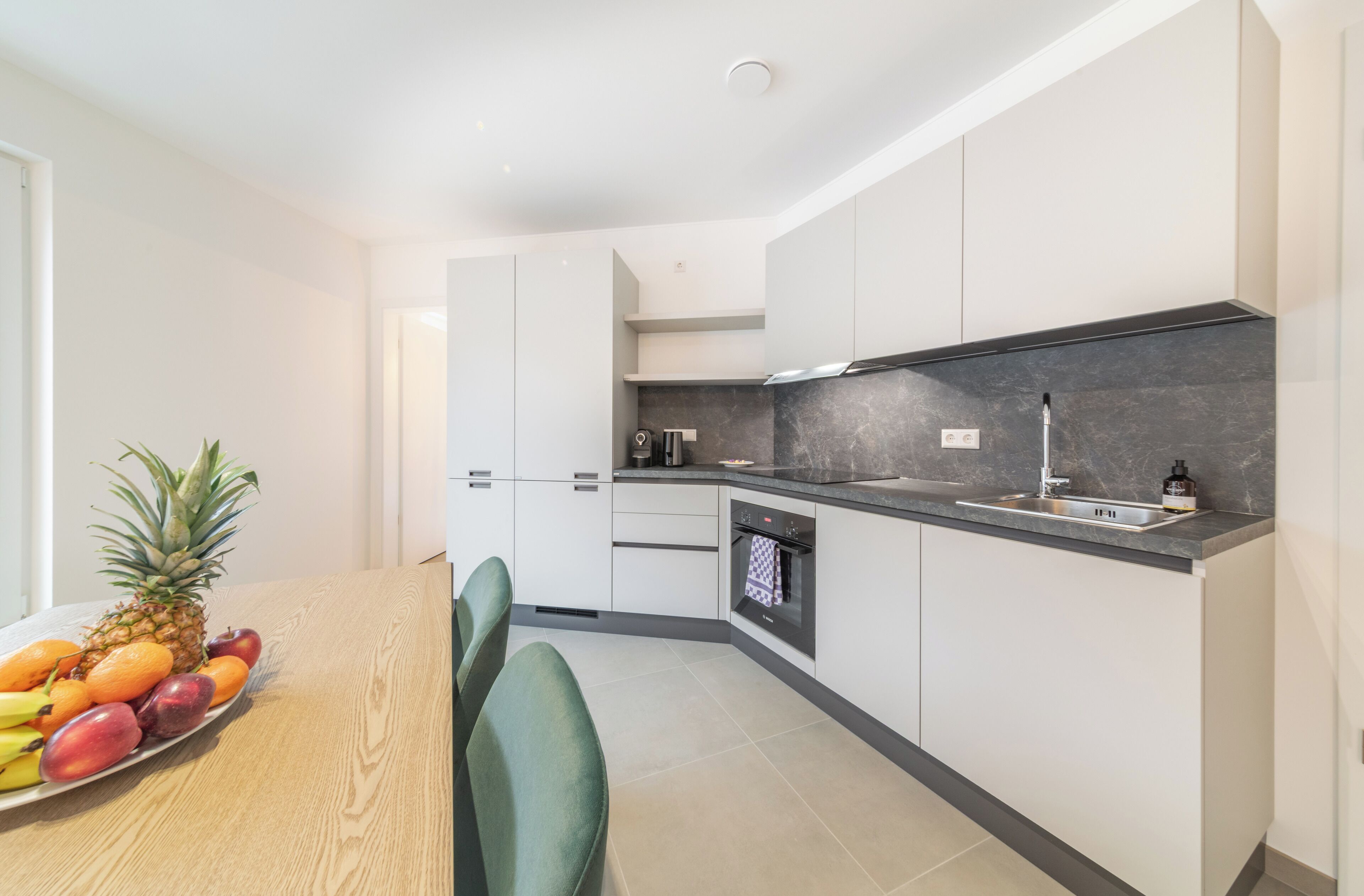 A modern kitchen with white cabinets, a black countertop, and a built-in oven.