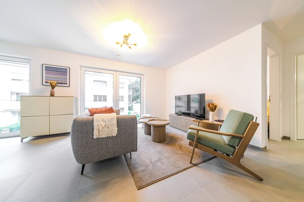 Una sala moderna con sofá, sillón verde, televisor y mueble.
