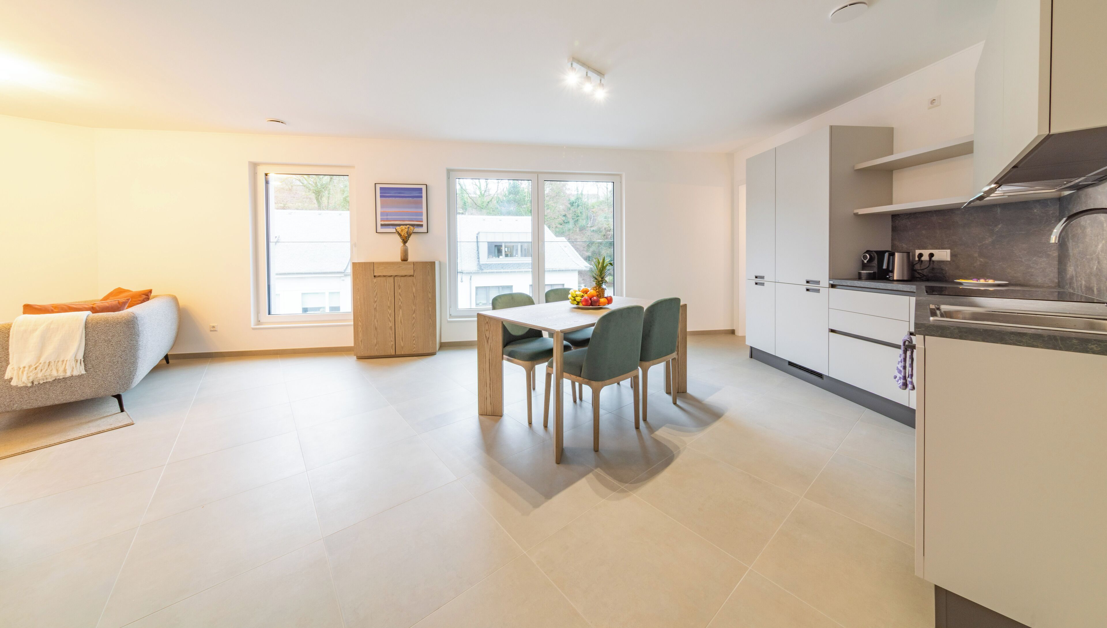 A modern kitchen with white cabinets, a dining table with chairs, and a sofa with a blanket.