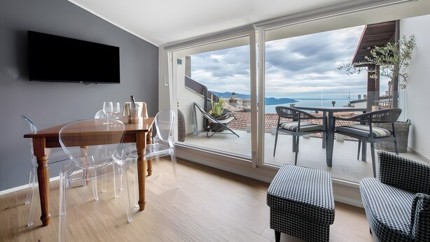 A modern room with a wooden dining table, clear chairs, a flat-screen TV, and a balcony with outdoor seating. - 'Piazzetta' Apartment with Balcony, Wi-Fi and Air Conditioning (Gardola)