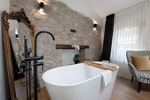 Ein modernes Badezimmer mit einer freistehenden Badewanne, einem großen Spiegel mit aufwendiger Rahmen und einer Wand aus Stein.