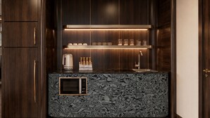 A modern kitchen with dark wood cabinetry, a marble-patterned countertop, a built-in microwave, and a shelf with glassware and a coffee maker. - The Prajan Hotel & Villas by Natt's (Yogyakarta)