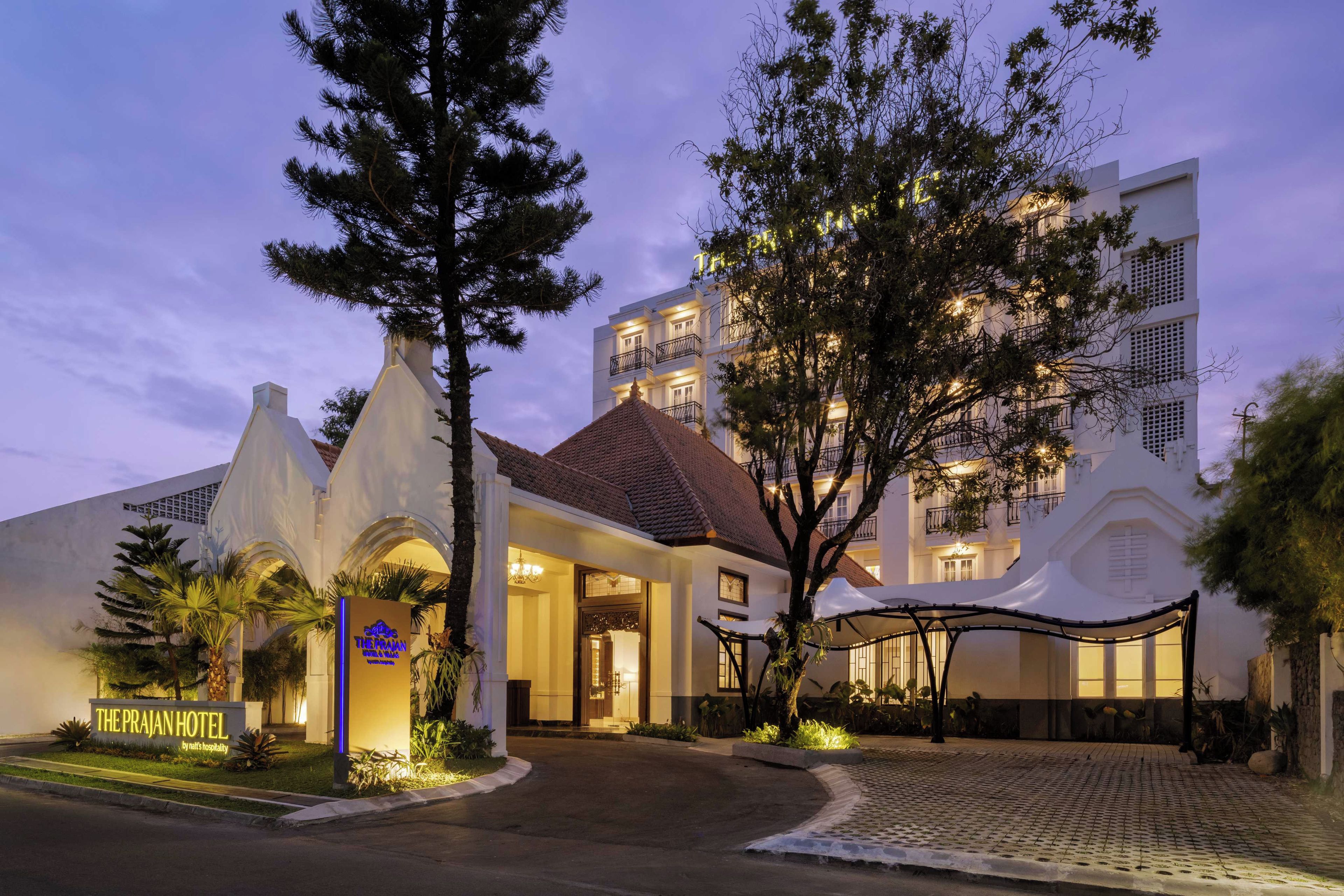 Ein Hotel Eingang mit einem modernen Gebäude im Hintergrund, einer Schautafel und einem gepflegten Garten.