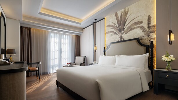 A hotel room with a large bed, a desk with a chair, a nightstand, and a wall-mounted lamp. - The Prajan Hotel & Villas by Natt's (Yogyakarta)