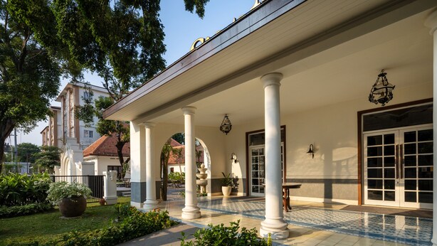 Un edificio con un porche cubierto, columnas, piso de baldosas y un jardín.