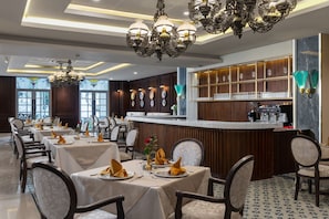 Un restaurante con varias mesas dispuestas para comer, una zona de bar y apliques decorativos en la pared.
