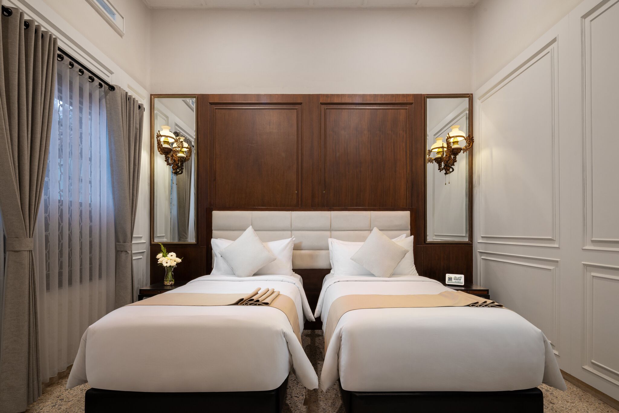 A hotel room with two beds, a large mirror, and a chandelier.
