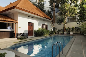 Una piscina con borde de azulejos, una puerta de madera y un edificio blanco con techo de tejas.