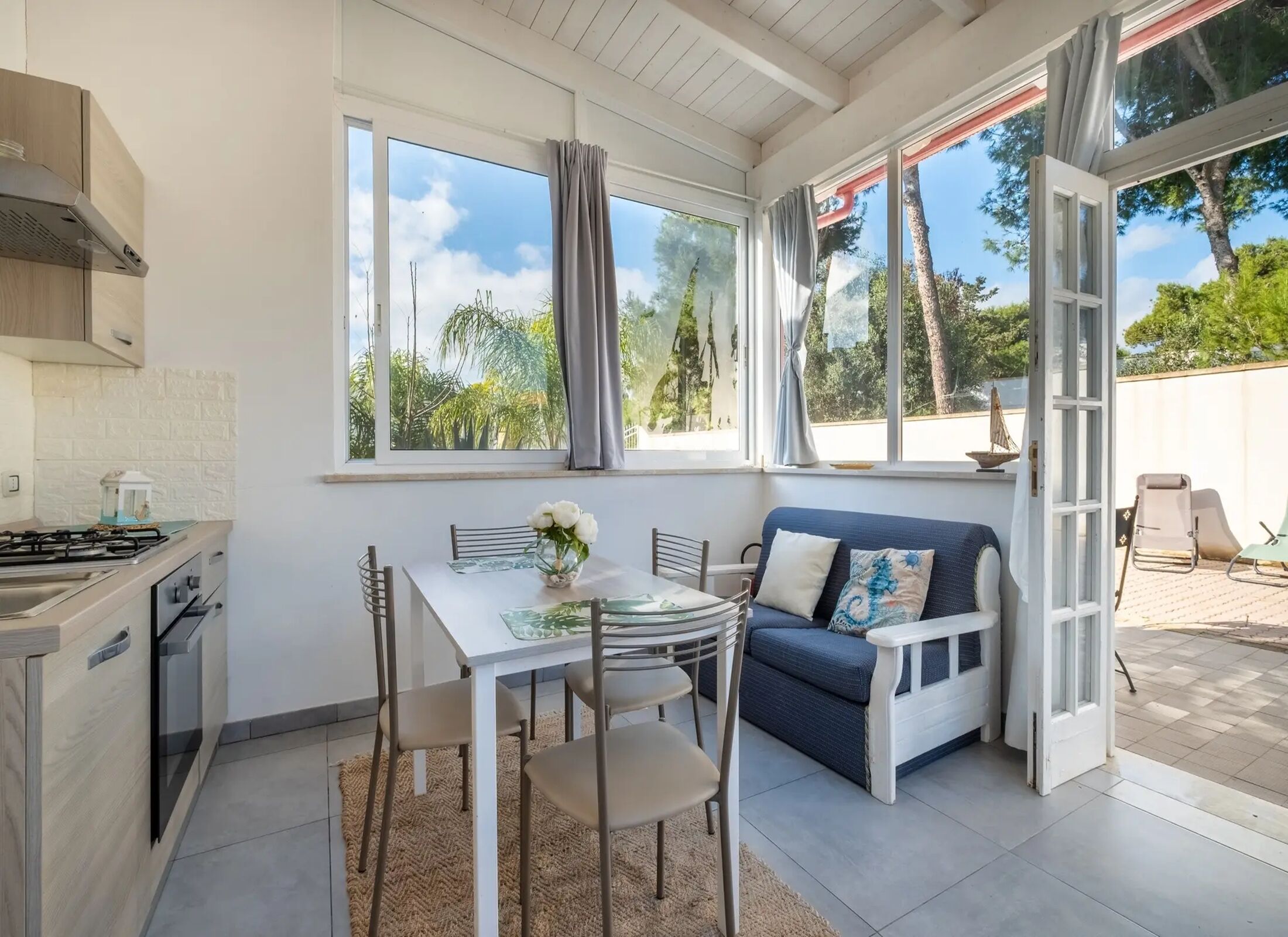 A modern kitchen with a dining area, large windows, and a view of the outdoors.