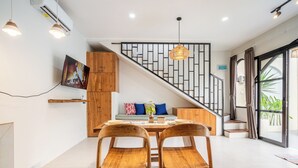Ein moderner Essbereich mit einem Holztisch und Stühlen, einer Treppe mit geometrischer Geländerkonstruktion und einem großen Fenster mit Vorhängen.