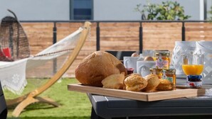 Ein Frühstücksarrangement mit Brot, Gebäck, Honig und Orangensaft auf einer Holzplatte.