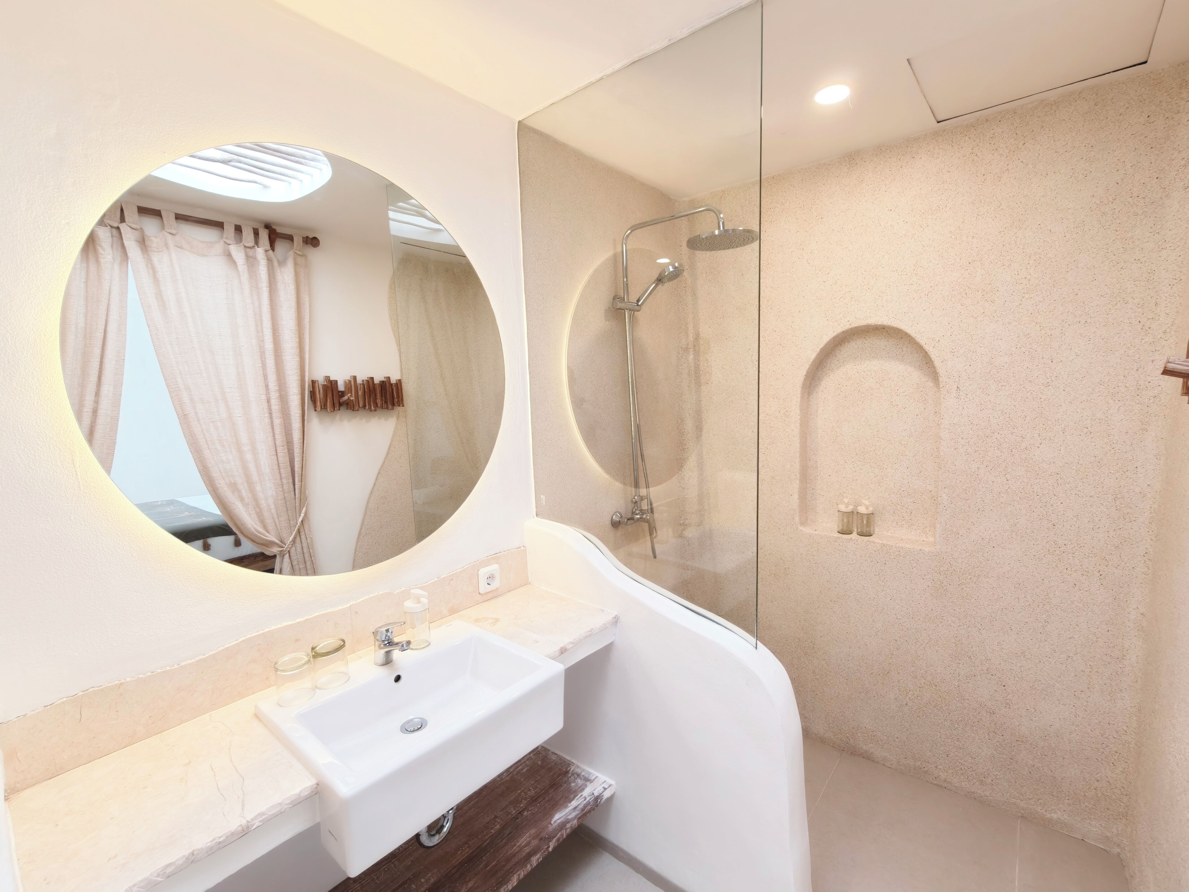 A modern bathroom with a round mirror, a white sink, and a glass-enclosed shower.