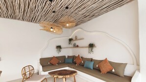 A modern living room with a curved sofa, a round wooden coffee table, and a wicker chair. There are hanging plants on shelves and a unique ceiling design. - Suilaya Villa Uluwatu (Pecatu)