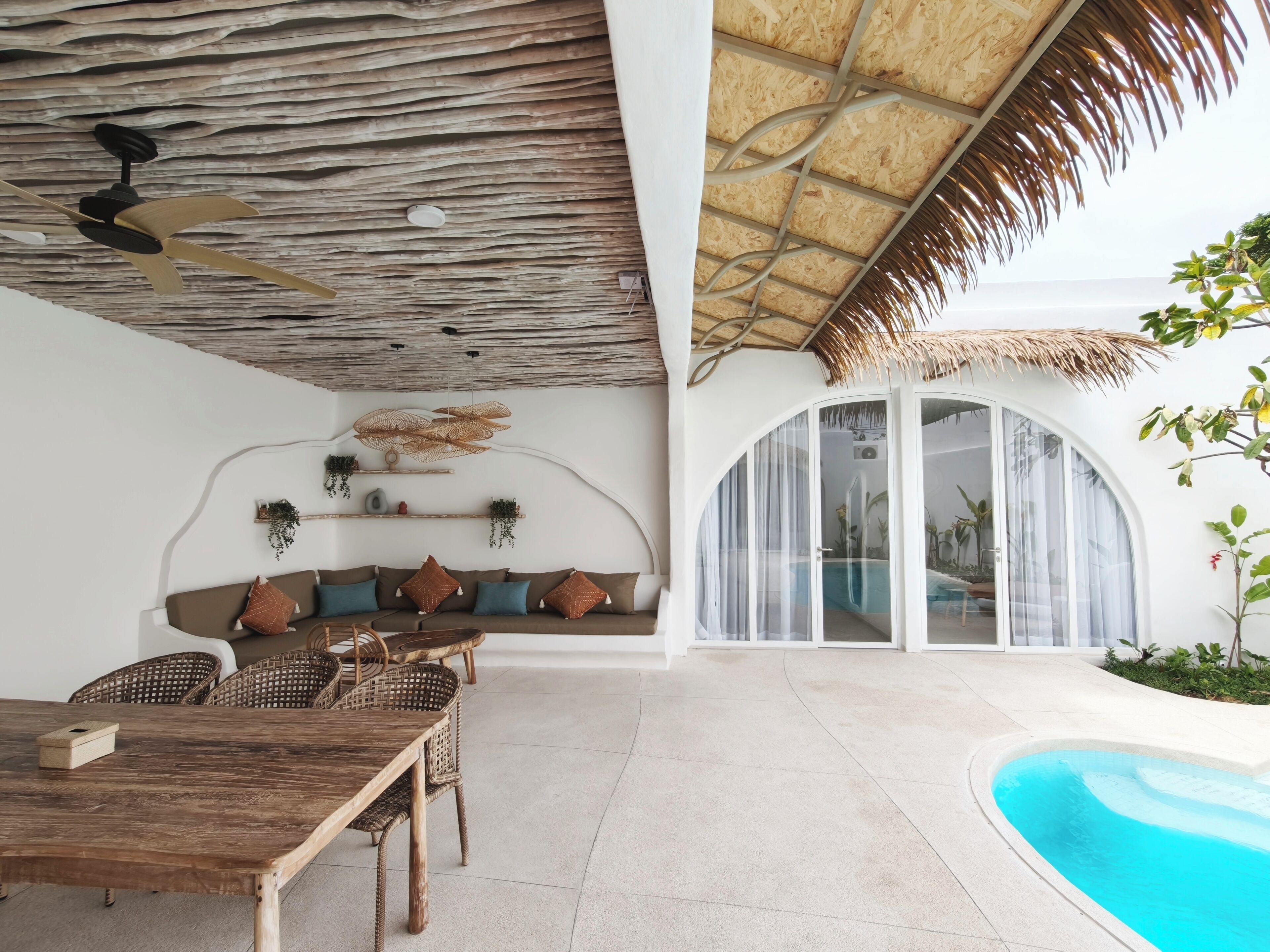 Un espace de vie extérieur moderne comprenant une piscine, une table à manger en bois et un coin salon avec des coussins.