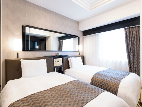Quarto de hotel com duas camas, um espelho grande, um painel de controle e uma janela com cortinas.