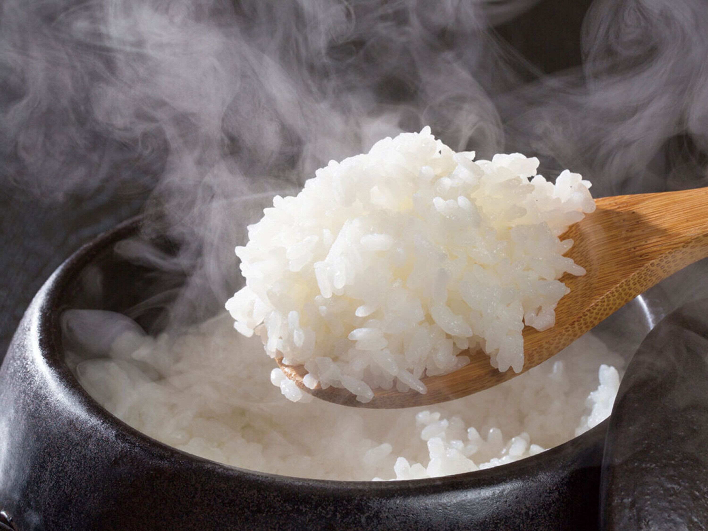 A wooden spoon holding cooked white rice over a pot.
