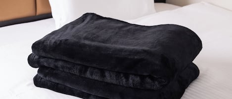 Una manta negra bien doblada sobre una cama con sábanas y almohada blancos.